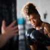 african woman boxing with punching bag in garage gym